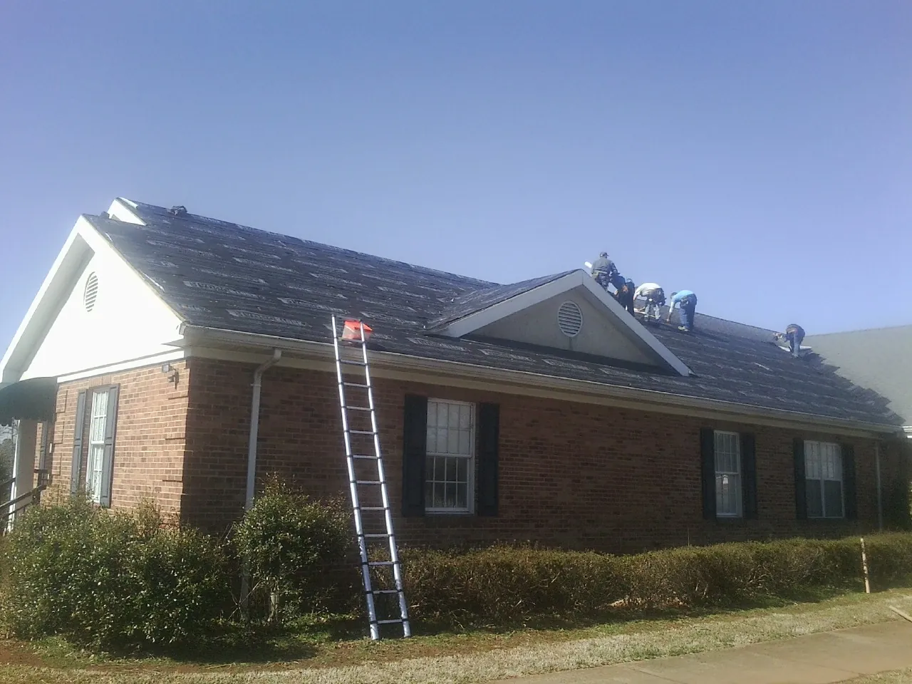 Crew tearing shingles off a brick ranch roof with a ladder set — Metal Roof Repair work by our crew in King And Queen Court House