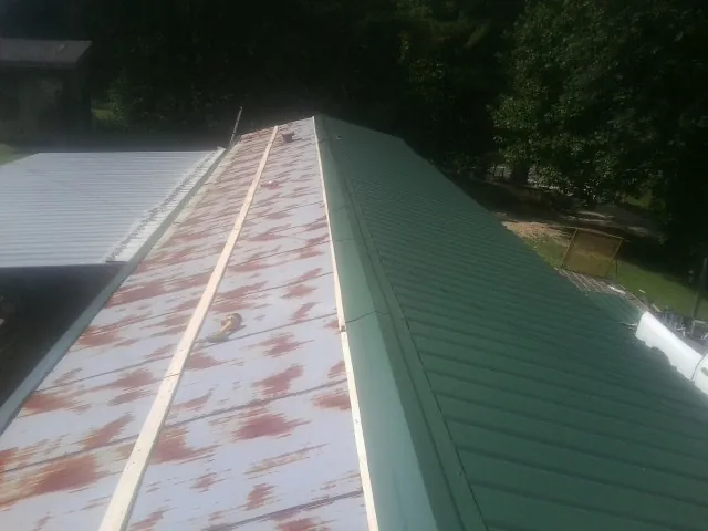 Old rusted panels beside newly installed green metal roofing — Wind Damage Roof Repair by Roofing Brothers in King And Queen Court House