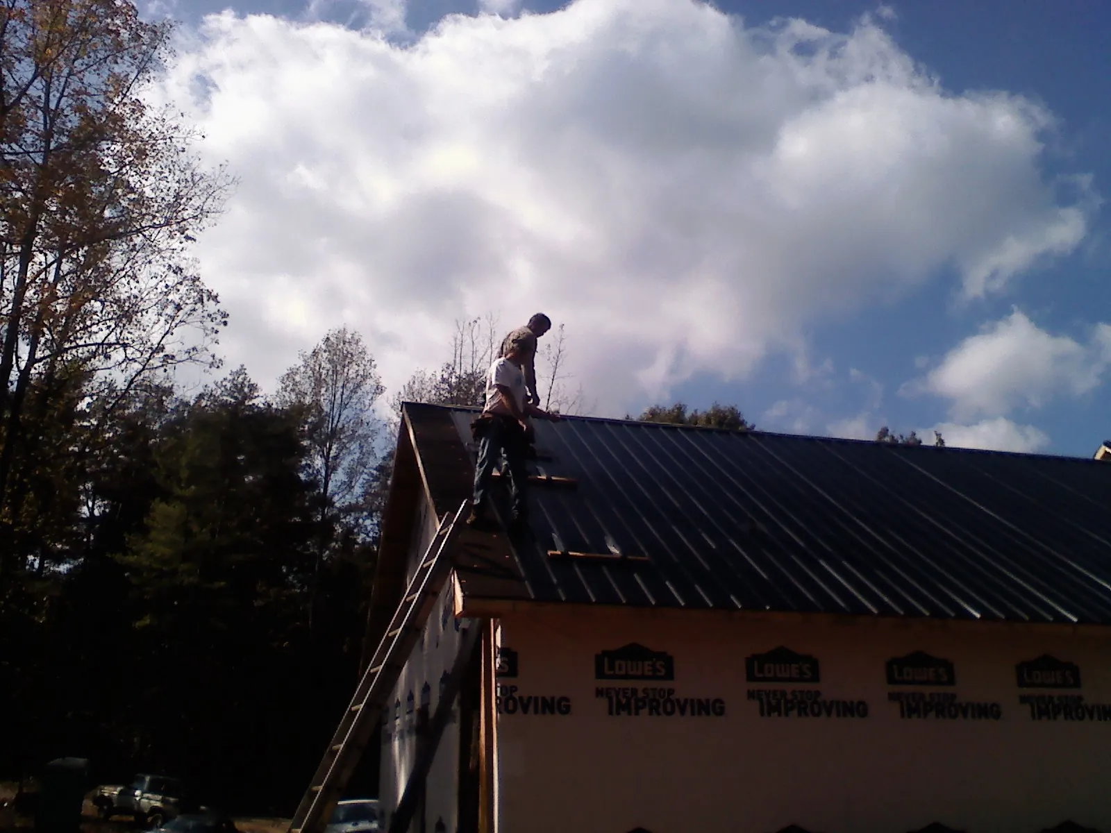 Roofer fastening dark metal panels high against a cloudy sky, from a Roof Inspection job in King And Queen Court House