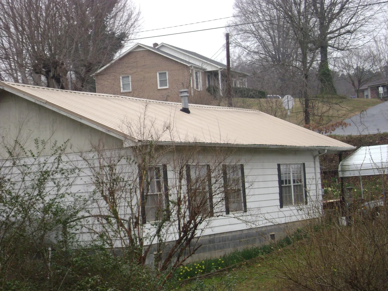 Tan metal roof on a white sided house set into a hillside — Commercial Roofing by Roofing Brothers in King And Queen Court House